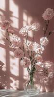 Delicate bouquet of white and pink carnations in glass vase against soft pink background photo