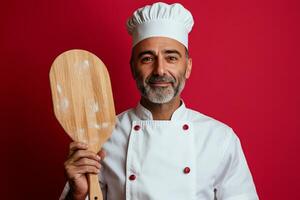 Chef holding wooden pizza peel against a red background in a professional kitchen photo