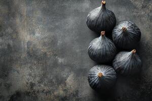 A pyramid of fresh dark figs arranged on a textured surface in a low light setting photo