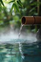 Tranquil bamboo water feature flowing into serene blue pond surrounded by lush greenery photo