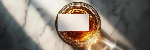A glass of amber liquid rests on a marble surface illuminated by soft sunlight photo