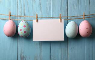 Colorful Easter eggs hanging on a string against a blue wooden backdrop with a blank card photo