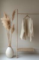 Cozy oversized sweater hanging near a modern decorative vase with dried plants in soft lighting photo