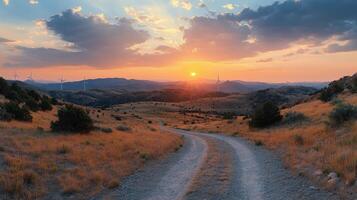 Sunset over rolling hills with wind turbines and a winding dirt road in the countryside photo
