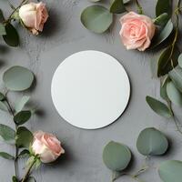 Circular blank canvas surrounded by pink roses and greenery on a textured gray surface photo