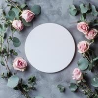 Circular blank canvas surrounded by pink roses and greenery on a textured gray surface photo