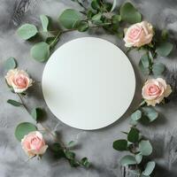 Circular blank canvas surrounded by pink roses and greenery on a textured gray surface photo