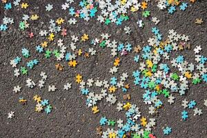 Colorful jigsaw. Unfinished scattered puzzle pieces spread on the gray asphalt pavement on the street. Messy chaotic concept. Close up. Selective focus. Blurred. photo