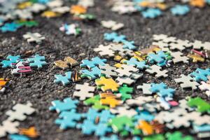 Colorful jigsaw. Unfinished scattered puzzle pieces spread on the gray asphalt pavement on the street. Messy chaotic concept. Close up. Selective focus. Blurred. photo