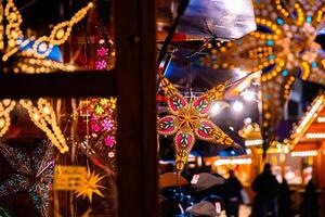 Rain speckled window showcasing illuminated colorful star lanterns glowing at Berlin Christmas market. Festive winter atmosphere with vibrant holiday lights photo