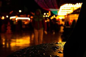 Rainy night at Christmas matket. Raindrops on a the table surface and blurry festive lights in the blurred background. Persons silhouette and distant people walking down the illuminated street photo