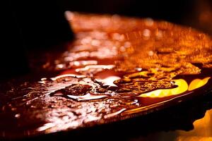 Close-up of water droplets on an street cafe table surface illuminated by warm golden light. glowing with warm orange and yellow tones, captured at night. Selective focus photo