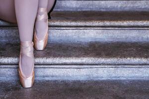 Ballerina in pink pointe shoes and white stockings sitting on stone steps capturing balance, grace, and calm. Closeup of dancer feet showing graceful ballet posture. photo