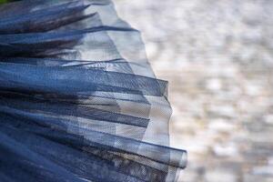 Closeup of delicate texture of a layered ballet tutu in soft, translucent fabric against a stone pavement background, symbolizing the grace and beauty of classical dance attire. photo