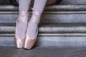 Ballerina in pink pointe shoes and white stockings sitting on stone steps capturing balance, grace, and calm. Closeup of dancer feet showing graceful ballet posture. photo