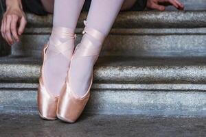 Ballerina in pink pointe shoes and white stockings sitting on stone steps capturing balance, grace, and calm. Closeup of dancer feet showing graceful ballet posture. photo