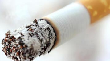 The tip of a burning cigarette covered in ash, quietly releasing wisps of smoke photo