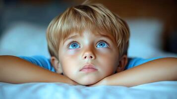 A young boy with striking blue eyes dreams while relaxing indoors photo