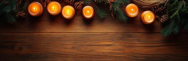 Candlelight and greenery on a wood table. Softly glowing candles surrounded by pine branches and pine cones create a cozy, festive atmosphere on a wooden surface. photo