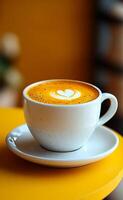A cup of coffee with a heart design on top sits on a yellow table. The coffee is hot and steaming, and the heart design adds a touch of warmth and affection to the scene photo
