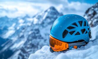 A blue helmet with orange goggles sits on top of a snowy mountain. The helmet is designed for extreme sports and is ready for use. Concept of adventure and excitement photo