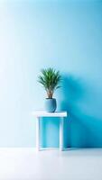 A small plant sits on a white table in front of a blue wall photo