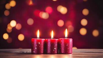 Three red candles on a wooden table with a blurred background photo