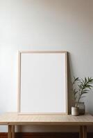 Mock up of a blank frame on a wooden table with a plant in front of it photo