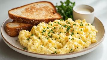 Scrambled eggs topped with chives and toasted bread on a plate for breakfast photo