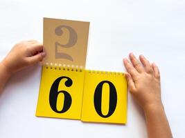Childs hands flip through yellow pages with numbers. Displaying number 60 on white background photo