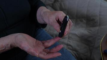 Elderly person's hands operating a compact glucometer while resting on living room sofa. Concept of diabetes management and at-home health monitoring for active seniors video