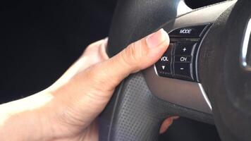 Hand presses the volume control button on a car steering wheel, adjusting the audio settings video