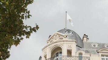 France, Paris - July 29, 2022. Bottom view of old European house with green tree. Action. Exterior of old building with Apple flag in Paris. House on Champs-Elysees with Apple Store video