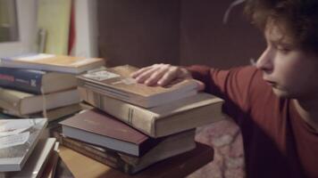 Tired student with bunch of books. Stock footage. Guy falls asleep on mountain of books. Young man is preparing for exams with books and wants to sleep video