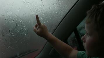 The child draws pictures with his finger on a wet misted window on a cloudy day. Creative. Boy drawing silhouette of a house. video