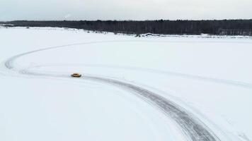 Aerial view of a driving car at snowy track at winter. Clip. One car driving through ice covered lake. video