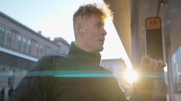 Cheerful young man dancing on street. Action. Young man is dancing merrily at bus stop on sunny day. Man in jacket and headphones dances while waiting for bus video