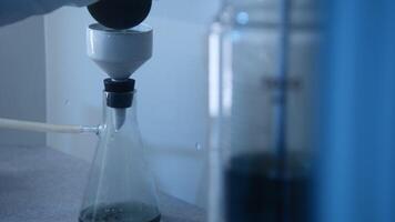 Chemist pours liquid into flask. Stock footage. Chemist conducts experiment with flask and liquid substance. Laboratory experiment with liquid and glass flasks video