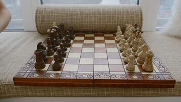 Child's hand makes chess move. Creative. Expensive chess board with pieces by window. Place on windowsill for relaxing with chess and child video