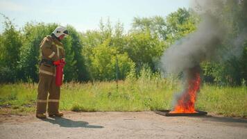 Fireman in helmet and protective uniform extinguishing the fire that bursting out from under the ground. Clip. Concept of saving lives, heroic profession, fire safety. video