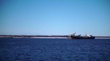 View of floating large vessel with cranes . Clip. Cargo ship with cranes floats on river on sunny day. Cargo ship sails on sunny winter day on background of snowy shore video