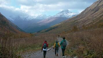 Rear view of a groupe of tourists exploring gorge between big mountain slopes. Creative. Autumn and cold mountain peaks on the background. video