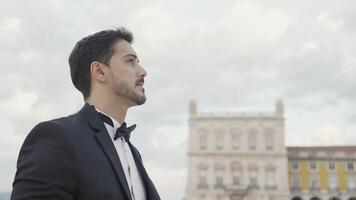 Handsome man in suit walks down street on summer day. Action. Attractive man in suit goes on date or event. Elegant man in suit walks confidently down street video