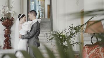 A couple of the bride and groom flirting with each other. Action. Smiling newlyweds filming in a building with bright lighting and decorations. video