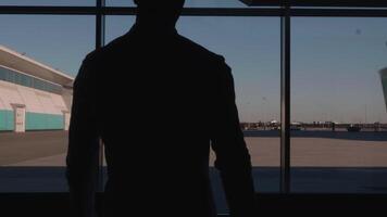A man walking down a corridor with large windows. HDR. A man in a shirt and jeans walks through the office where a beautiful evening sunset is visible. video