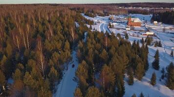 Top view of snowmobile and village in forest in winter. Clip. Cinematic view of snowmobile going to old village. Snowmobile in forest on background of village and mountains in winter video