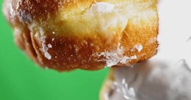 Donut with dripping white icing. Stock clip. Close-up baking with stream of white cream. White cream drips from bun on green background. Baking and cooking video