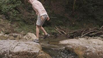 Legs of a boy jumping trough a creek in slow motion. Creative. Boy and mountainous cold stream. video