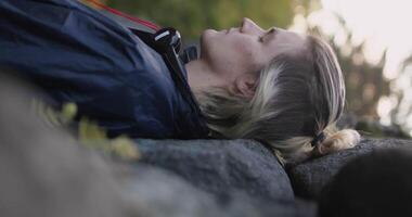 Man lying on stones with closed eyes with blurred forest leaves on the background. Stock. Man relaxing in nature. video