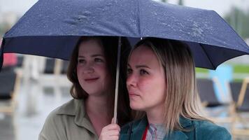 Two women joyfully sharing an umbrella while standing together in the rain and sharing a moment. Clip video